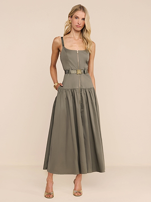 A woman wears the Rima Dress—an olive green, square-neck midi with adjustable straps and a belt—paired with gold sandals. Her long wavy blonde hair and minimal jewelry complete the look against a plain light background.
