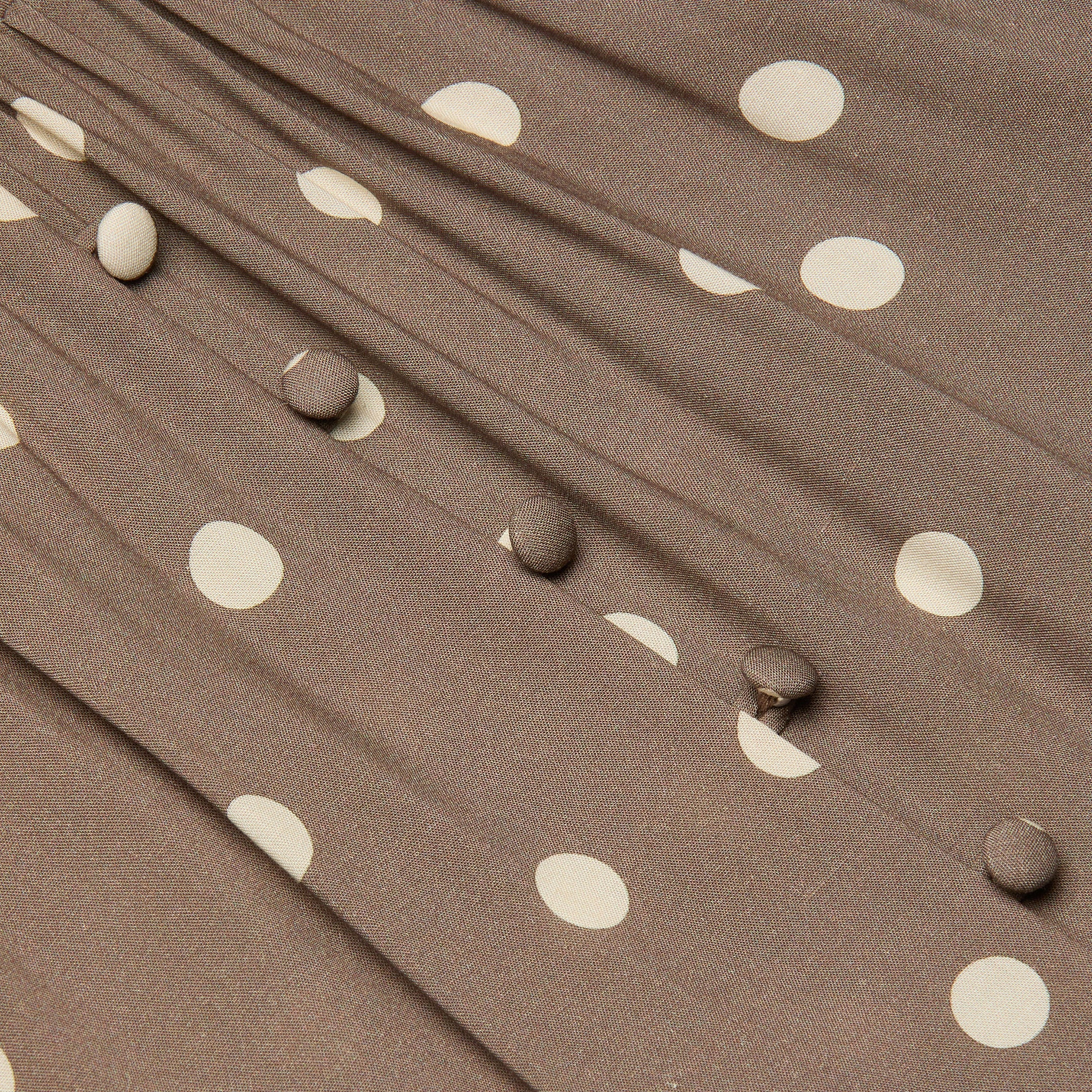 Close-up of the Rosette Maxi Dress featuring brown fabric with white polka dots, fabric-covered buttons in a row, and gathered pleats that highlight its summer-ready style.