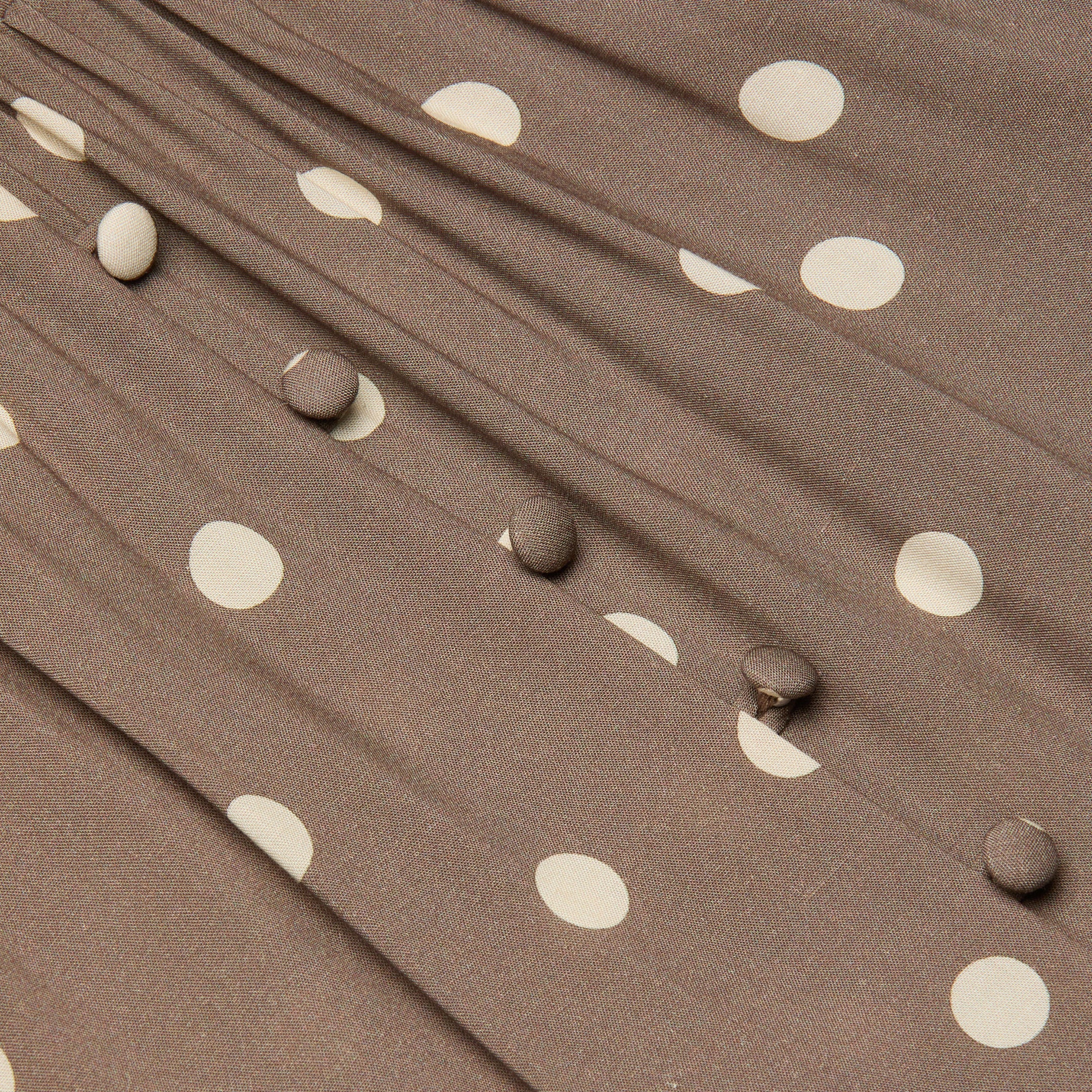 Close-up of the Rosette Maxi Dress featuring brown fabric with white polka dots, fabric-covered buttons in a row, and gathered pleats that highlight its summer-ready style.