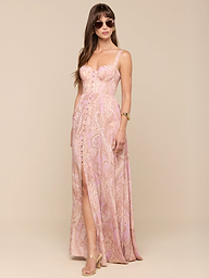 A woman stands against a plain white background wearing the Rosette Maxi Dress—a mauve paisley, sleeveless maxi dress with a thigh-high slit—paired with sunglasses, gold heels, and a watch.