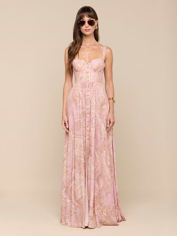 A woman with long brown hair stands facing forward against a plain white background, wearing sunglasses and the Rosette Maxi Dress—a long, mauve paisley maxi dress. Her arms are relaxed at her sides.