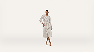 A woman stands confidently wearing a long-sleeved, belted, white midi dress with a subtle floral pattern and open-toe heels against a plain white background.