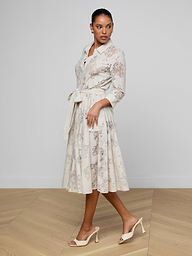 A woman is wearing the Ralphie Lace Midi Dress, featuring a classic silhouette with long sleeves, a belted waist, and a delicate floral pattern. She completes the look with light heels and stands against a plain white background.