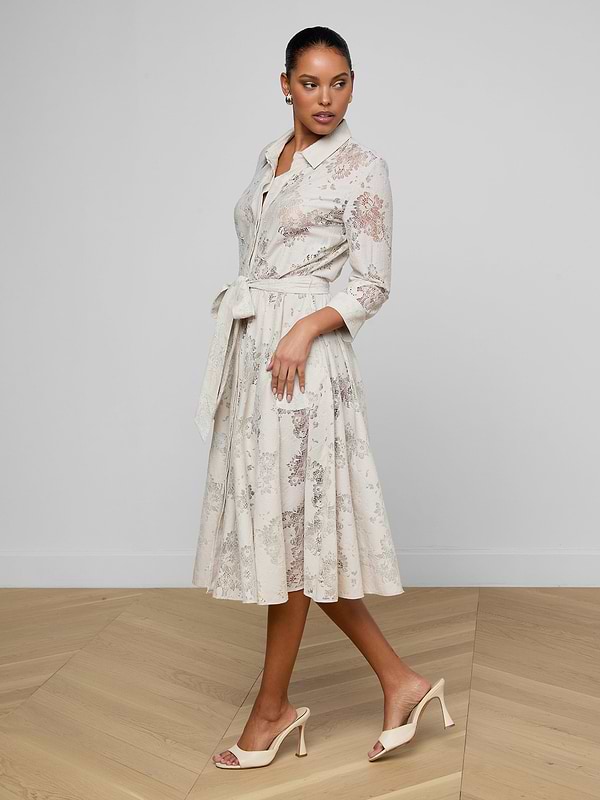 A woman wears the Ralphie Lace Midi Dress, featuring a light pattern, tie waist, and three-quarter sleeves, paired with beige heeled sandals. She stands on wooden flooring against a plain white background.