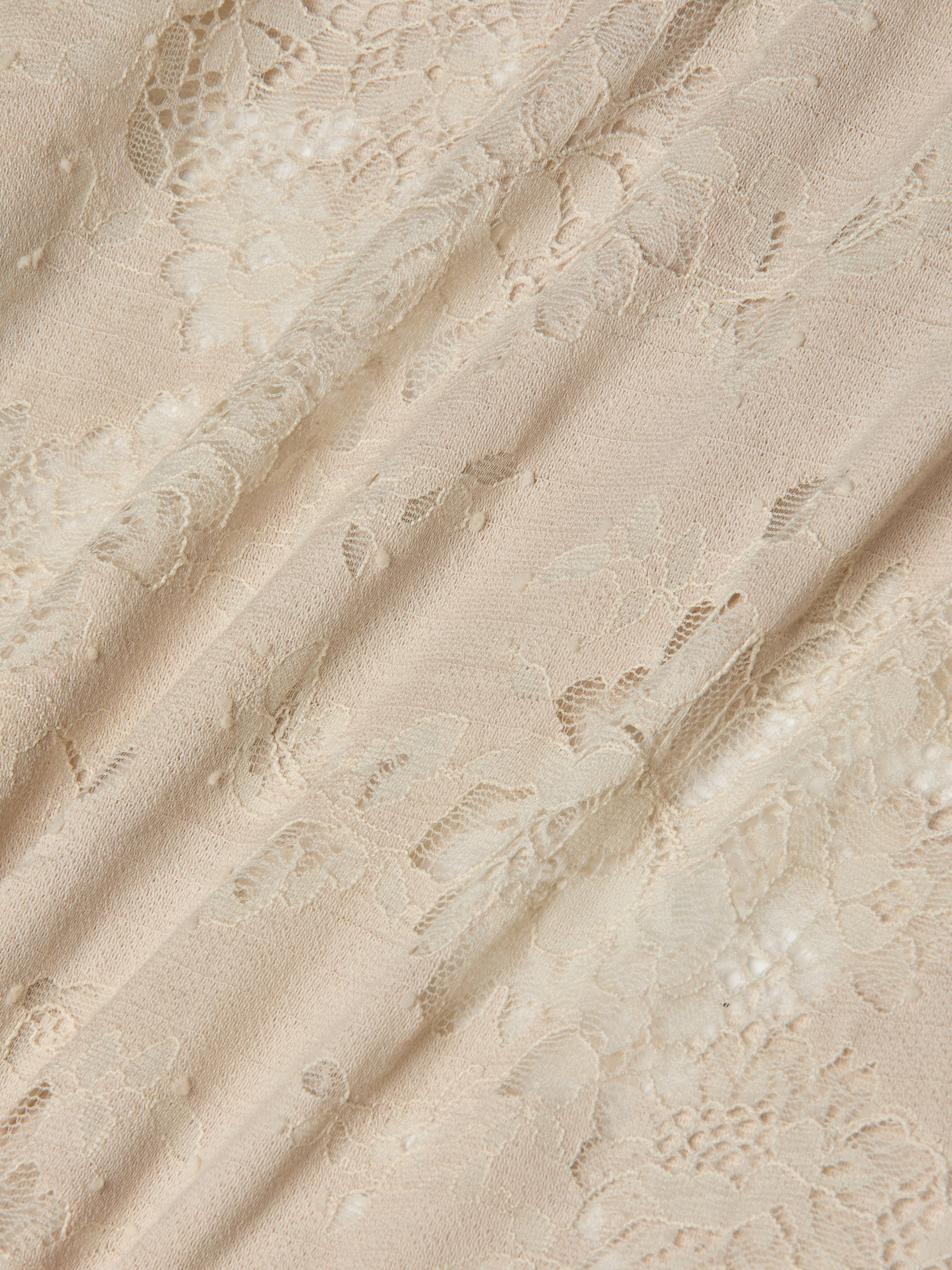 Cream-colored lace fabric with a delicate floral pattern, draped softly to highlight its texture and semi-transparency, evokes the intricate details and subtle sheen of the Ralphie Lace Midi Dress.