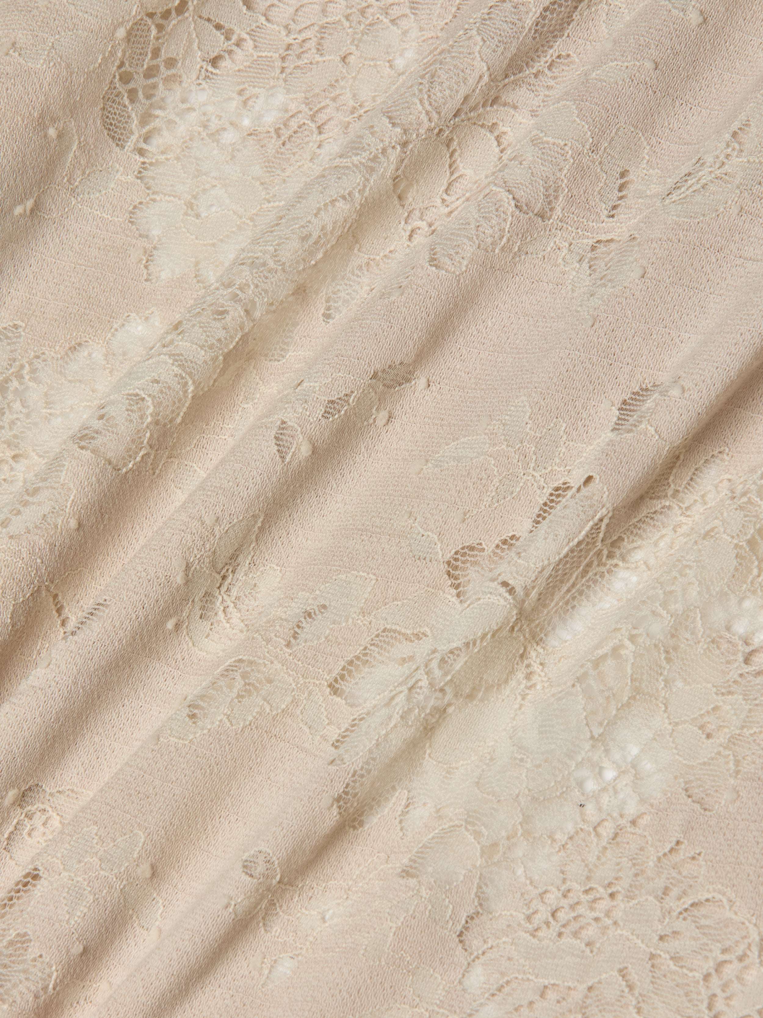 Cream-colored lace fabric with a delicate floral pattern, draped softly to highlight its texture and semi-transparency, evokes the intricate details and subtle sheen of the Ralphie Lace Midi Dress.