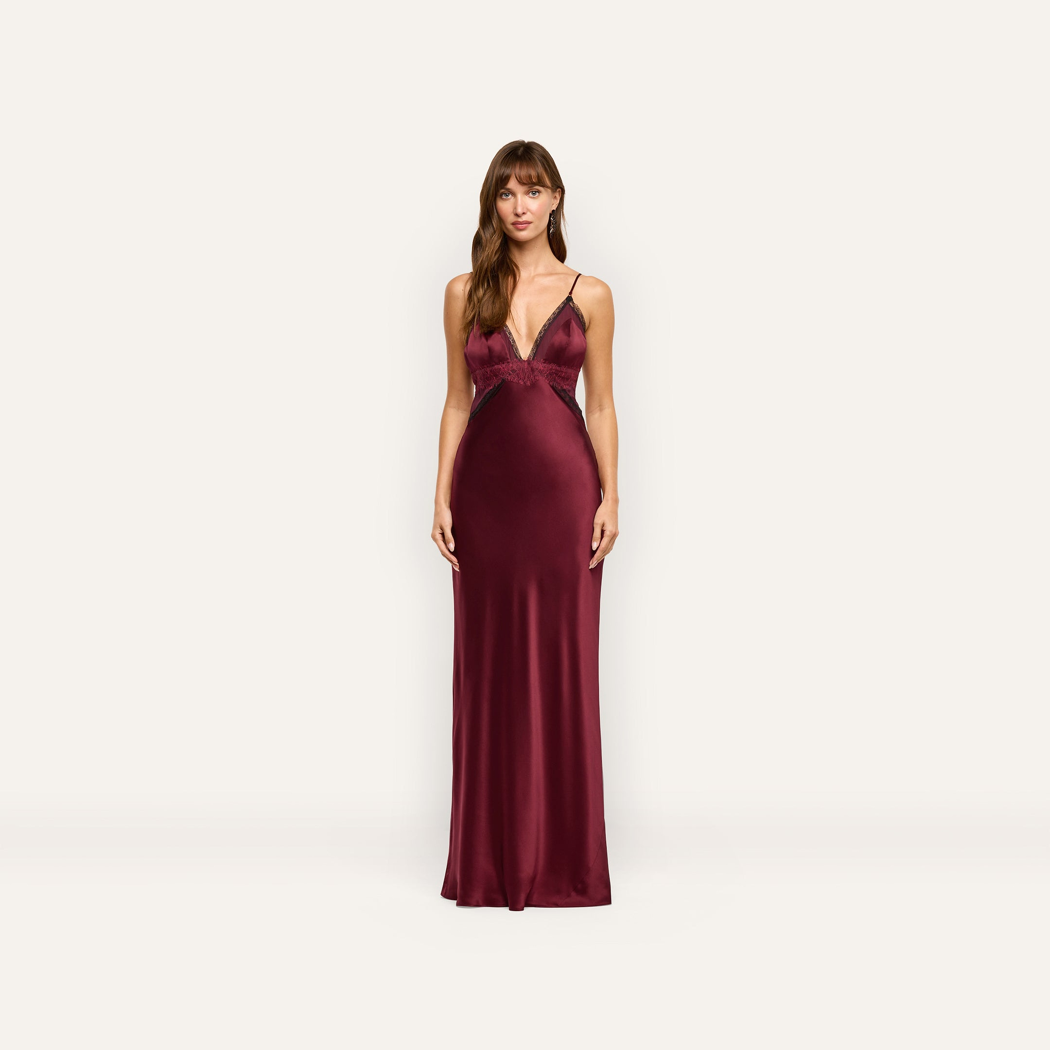 A woman wearing the Elsa Silk Gown, a floor-length, deep red silk slip dress with black lace accents at the neckline and waist.