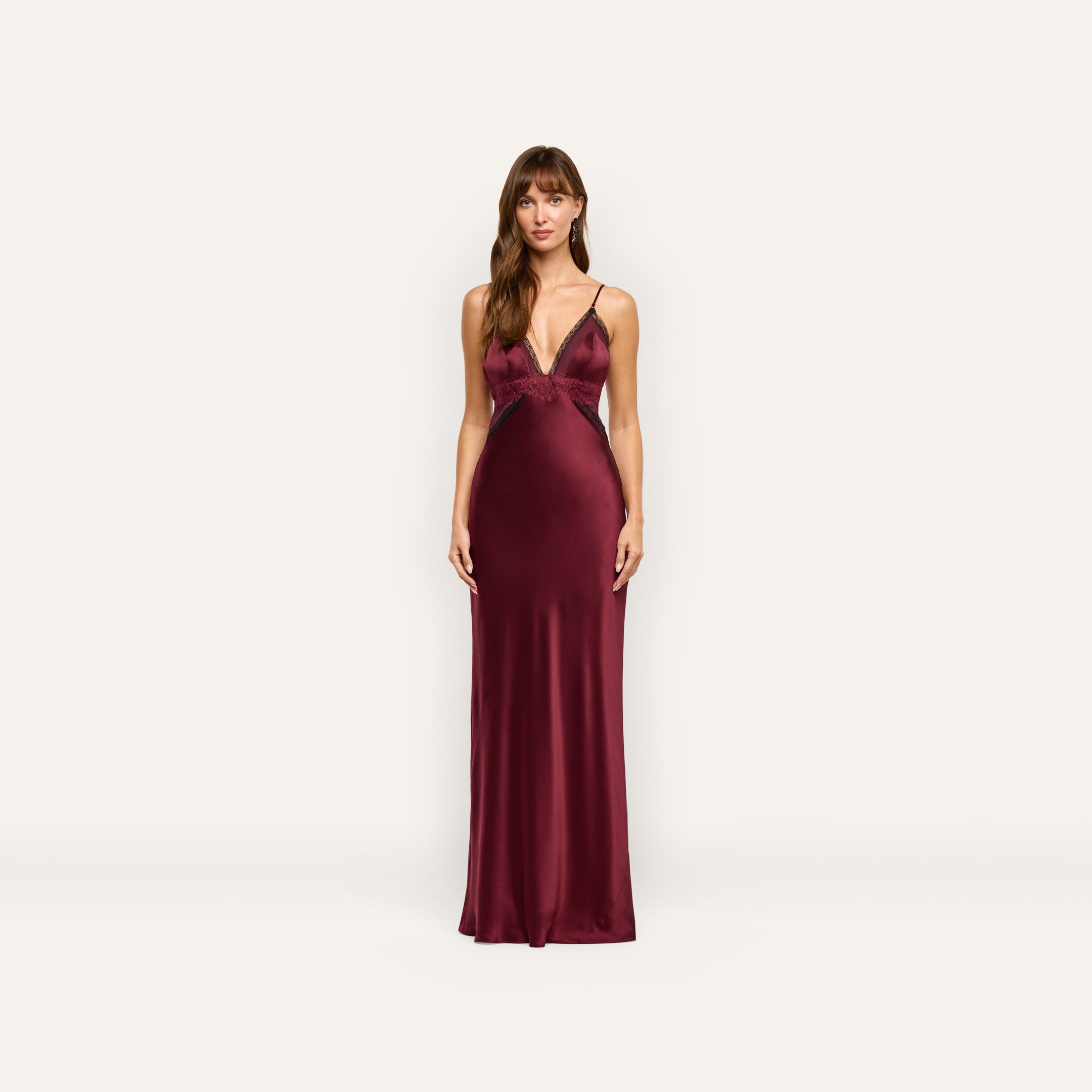 A woman wearing the Elsa Silk Gown, a floor-length, deep red silk slip dress with black lace accents at the neckline and waist.
