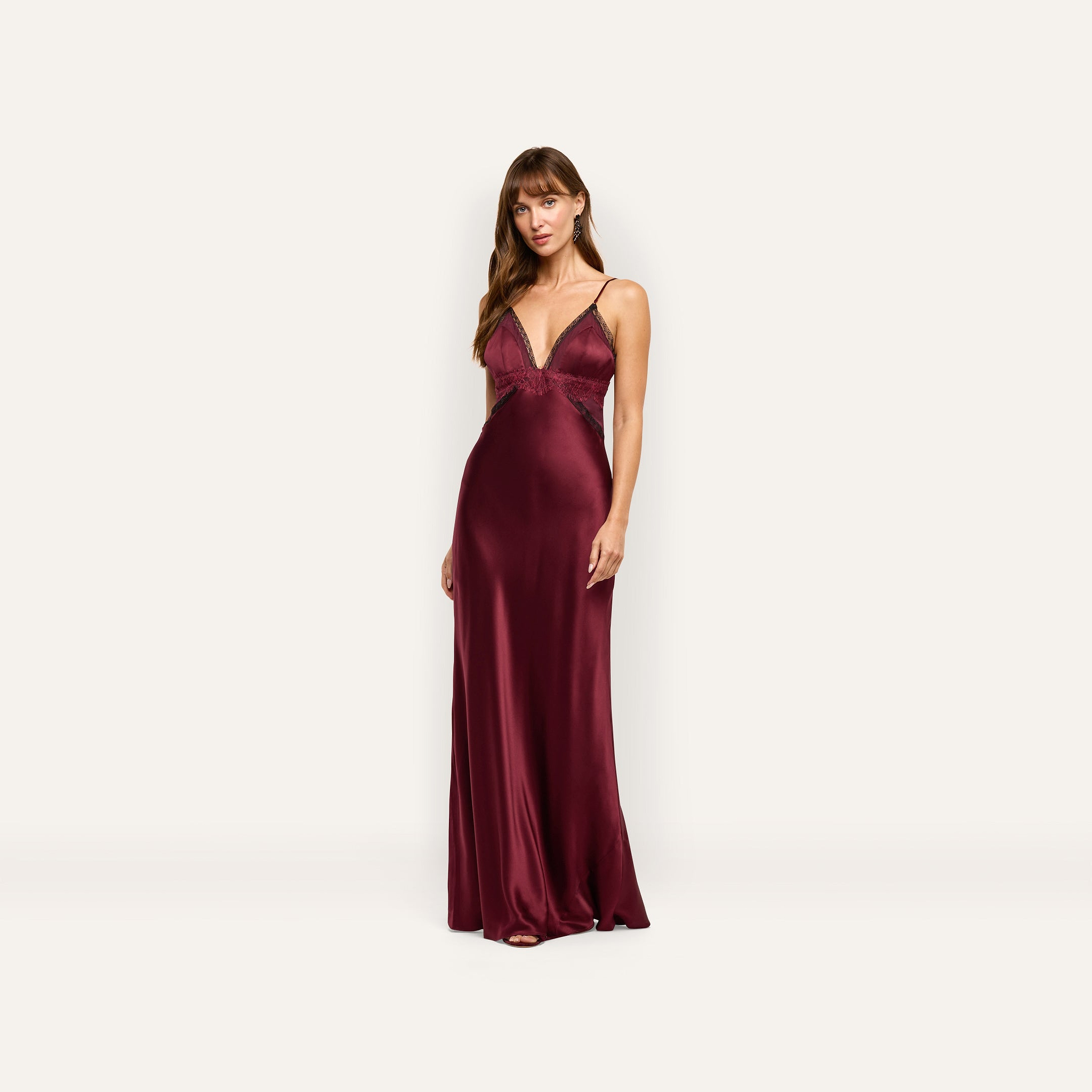 A woman wearing an Elsa Silk Gown, a floor-length, deep red silk slip dress with a V-neckline and delicate lace accents.