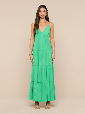 A woman with long brown hair wears the Lua Tiered Maxi Dress—bright green, crinkle-effect satin with adjustable straps and a tiered skirt—against a beige background, styled with neutral sandals and minimal jewelry.
