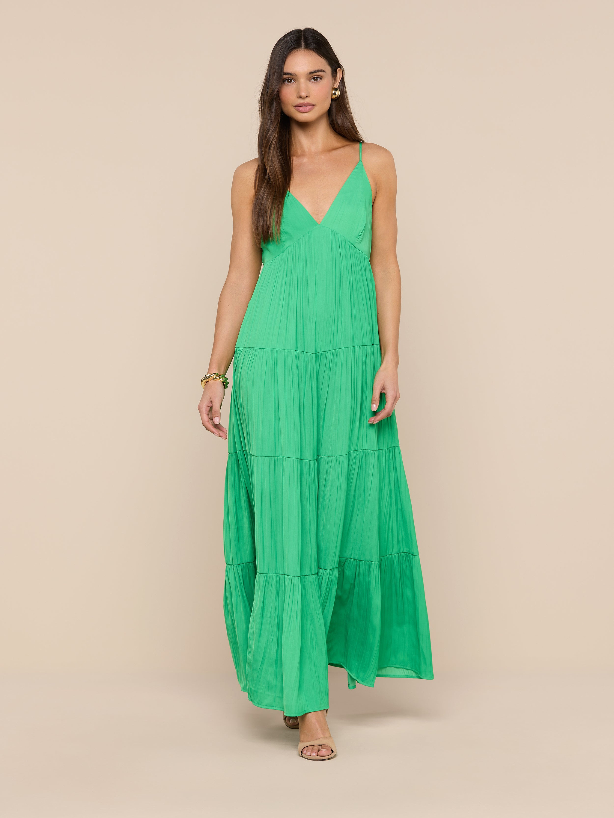 A woman in the Lua Tiered Maxi Dress—a sleeveless, long green maxi dress with adjustable straps—stands facing forward against a plain white background. The crinkle-effect satin fabric adds subtle texture to the elegant look.