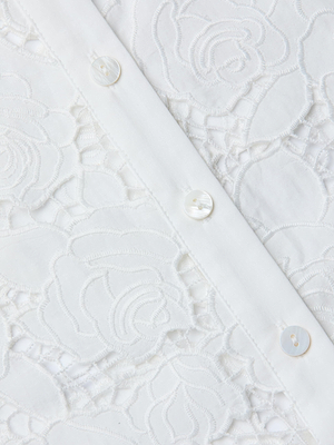 Close-up of the May Eyelet Shirt Dress, a white cotton midi featuring intricate floral lace embroidery and leaves, with a vertical row of white buttons on a plain strip—perfect for summer.