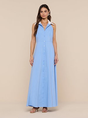 A woman with long brown hair and nude heels stands against a beige background wearing the Maurie Poplin Maxi Dress, a sleeveless light blue organic cotton poplin maxi dress with a white collar and button-down front.