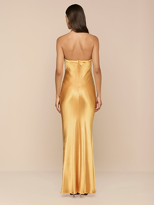 Une femme aux longs cheveux bruns est de face, portant la robe Saphara Halter Gown - une robe de satin longue comme le sol, avec un soutien-gorge intégré. Le fond beige uni met en valeur la finition lisse et brillante de la robe.