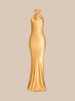 La robe dos nu Saphara est une robe en satin doré avec un col dos nu et un soutien-gorge intégré. Elle présente un corsage ajusté et une jupe légèrement évasée qui descend jusquau sol, sur un fond beige uni.
