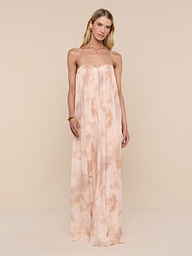 A woman stands against a plain white background wearing the Raine Strapless Gown, featuring flowing peach and cream tie-dye fabric and a built-in corset.