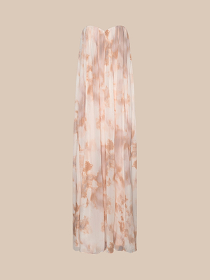 The Raine Strapless Gown is a floor-length dress with a built-in corset and a pleated, flowing silhouette in soft beige and peach tie-dye hues, shown against a plain beige background.
