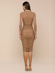 Una mujer mira hacia otro lado, con el vestido Adriana Ruched Midi Dress -ajustado, de manga larga y color canela- combinado con tacones altos sobre un fondo beige liso.