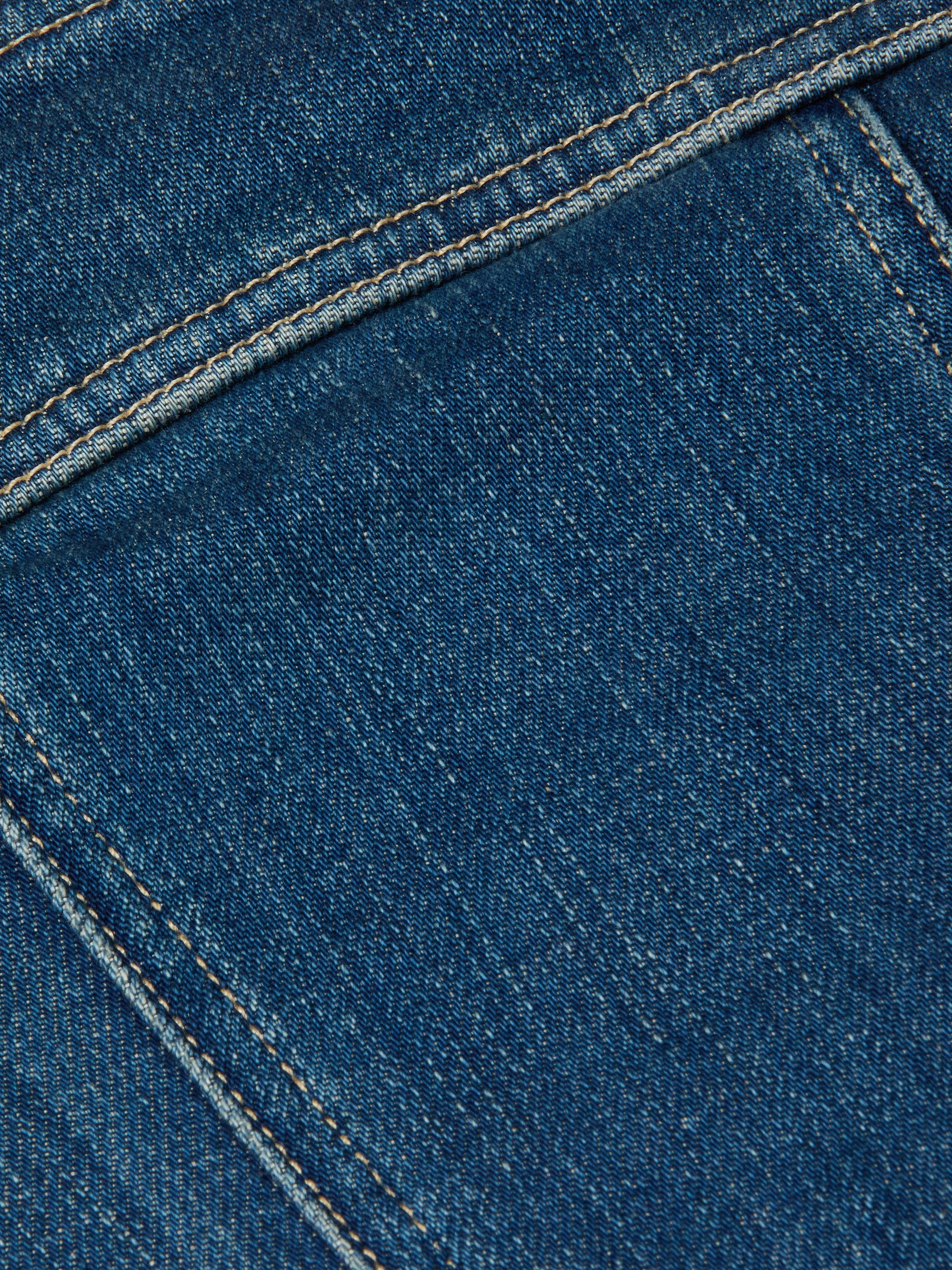 Close-up of the Lorda Dress in blue stretch denim fabric, highlighting detailed stitching, textured material, visible seams, and yellowish thread.