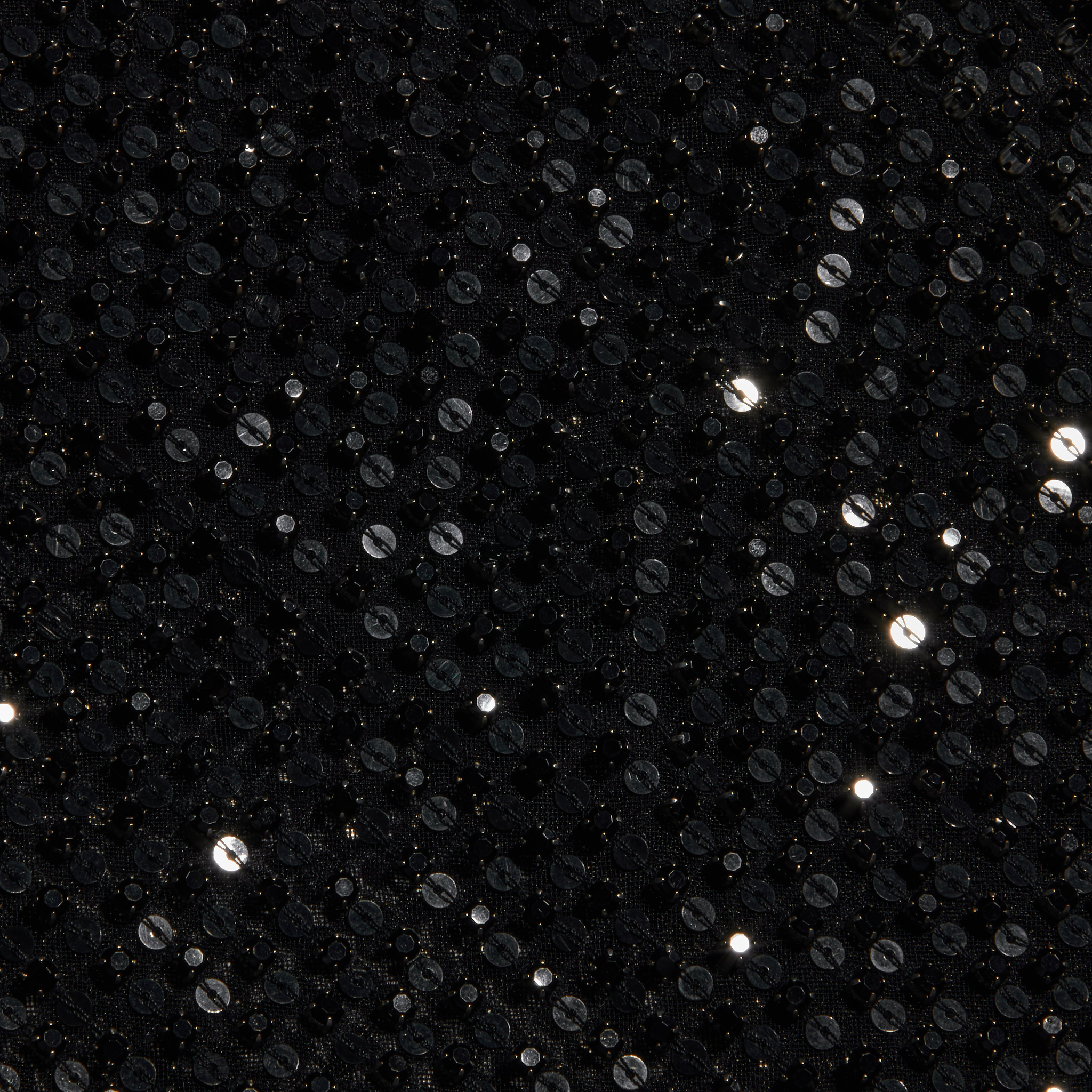 Close-up of the Paula Gown’s black sequin fabric, featuring small, round, shiny sequins that reflect light and create sparkling highlights on a dark textured background—perfect for adding a touch of glamour to sheer mesh eveningwear or pairing with sequin rhinestone embellishments.