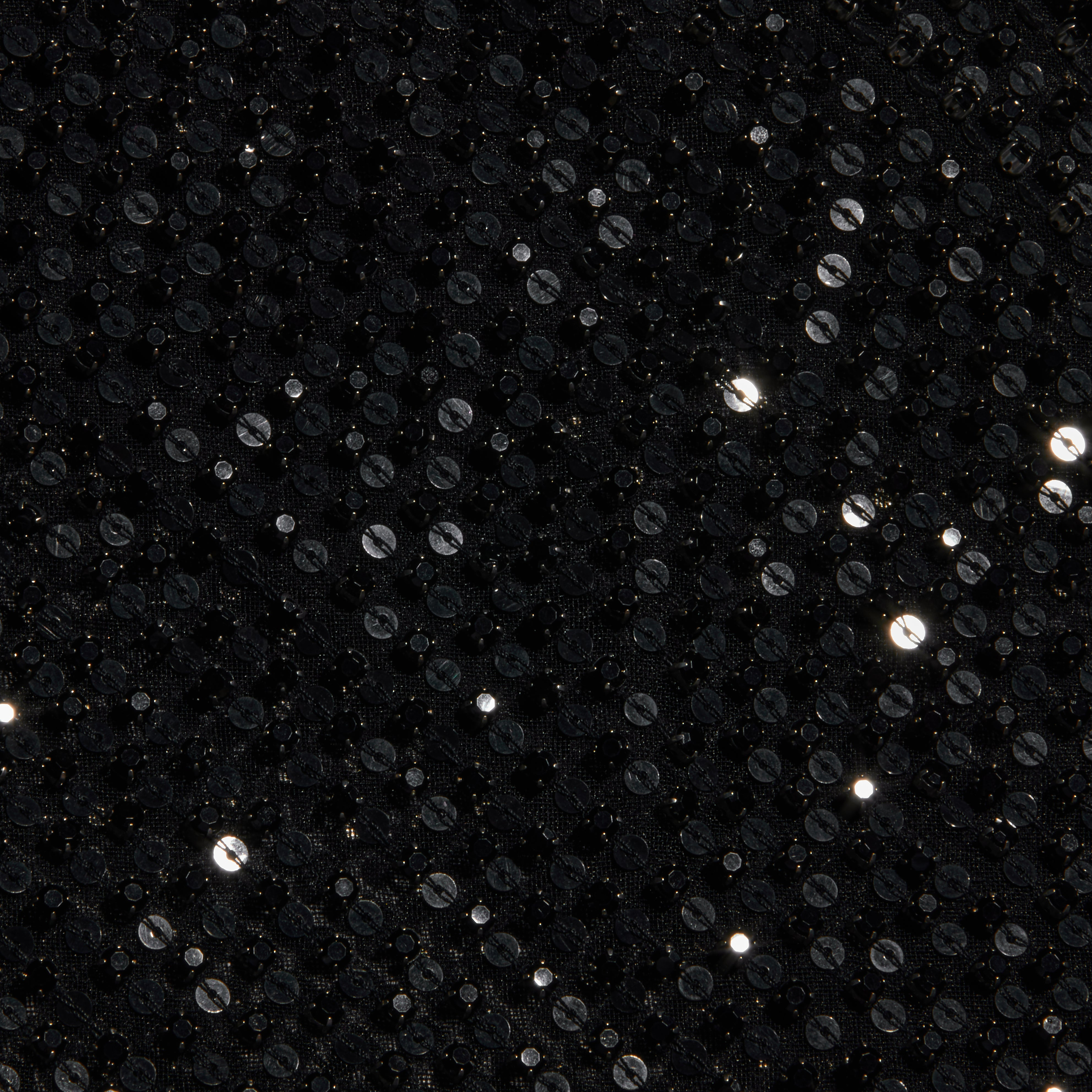 Close-up of the Paula Gown’s black sequin fabric, featuring small, round, shiny sequins that reflect light and create sparkling highlights on a dark textured background—perfect for adding a touch of glamour to sheer mesh eveningwear or pairing with sequin rhinestone embellishments.
