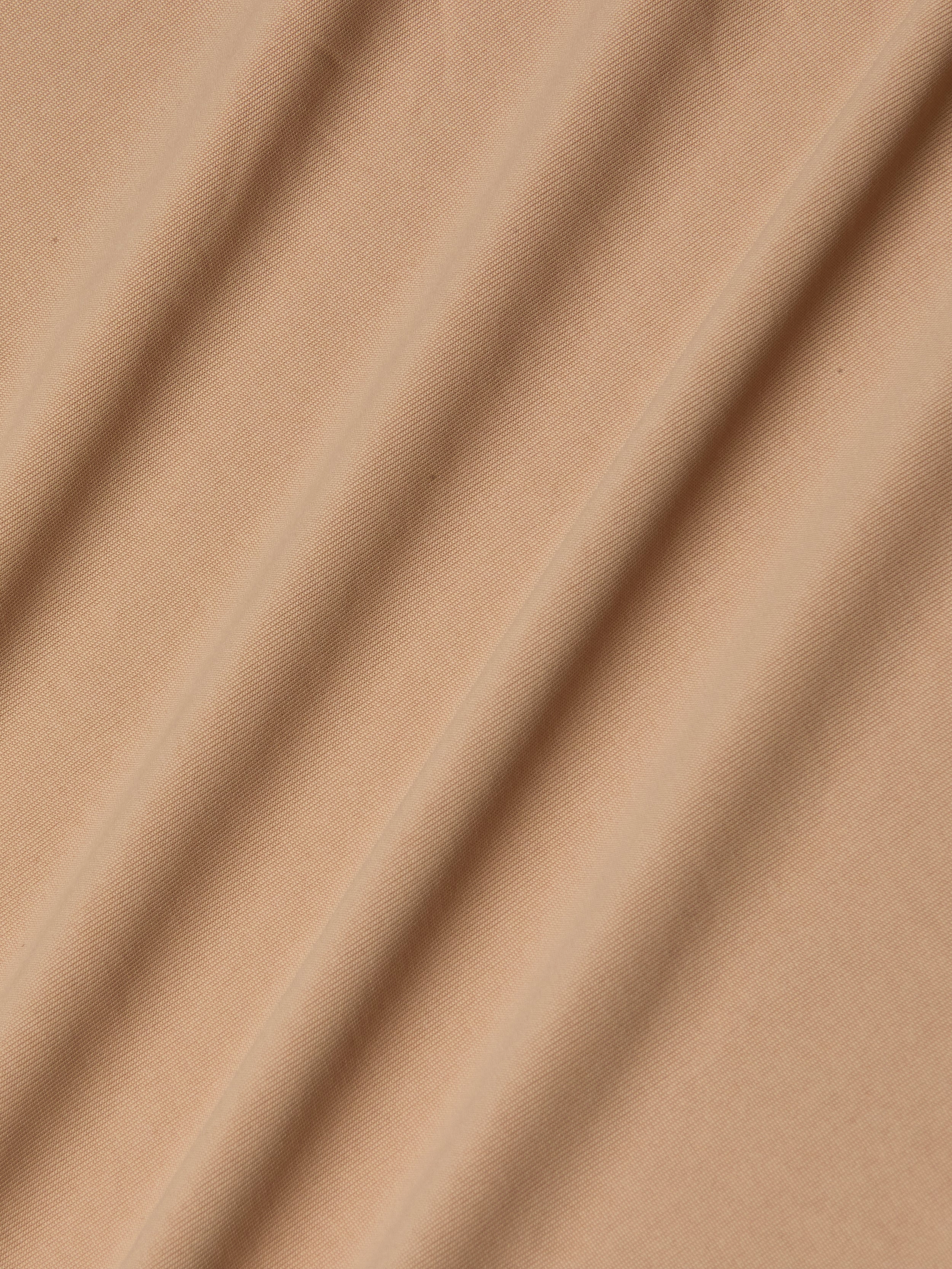 Light brown stretch jersey fabric forms the Raye Slip Lining Dress, its softly draped folds lending gentle shadows and textured dimension across the surface.