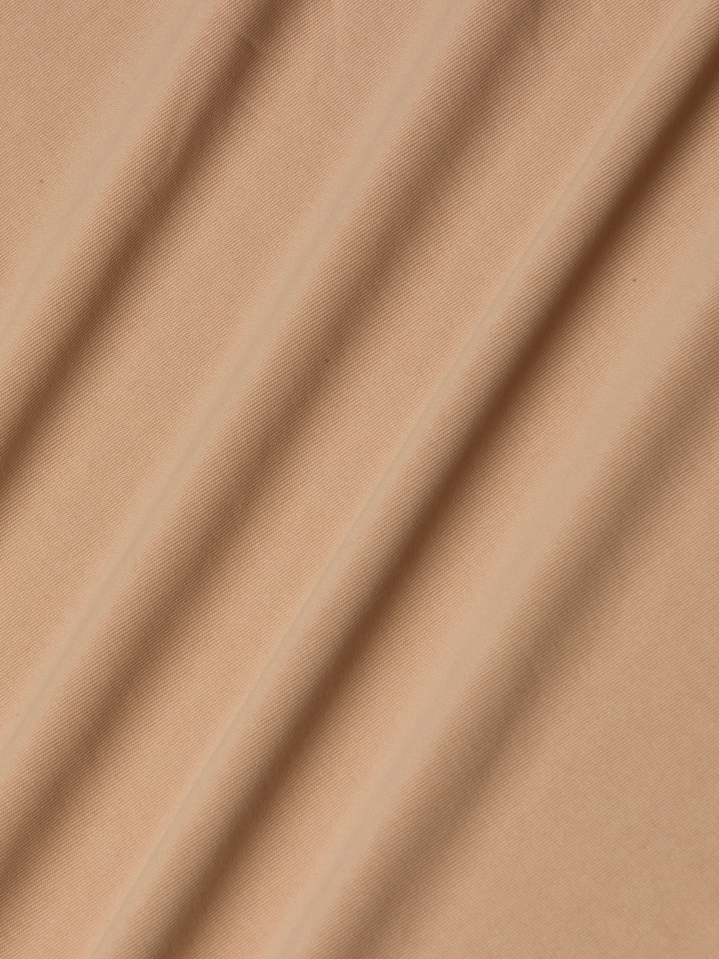Light brown stretch jersey fabric forms the Raye Slip Lining Dress, its softly draped folds lending gentle shadows and textured dimension across the surface.