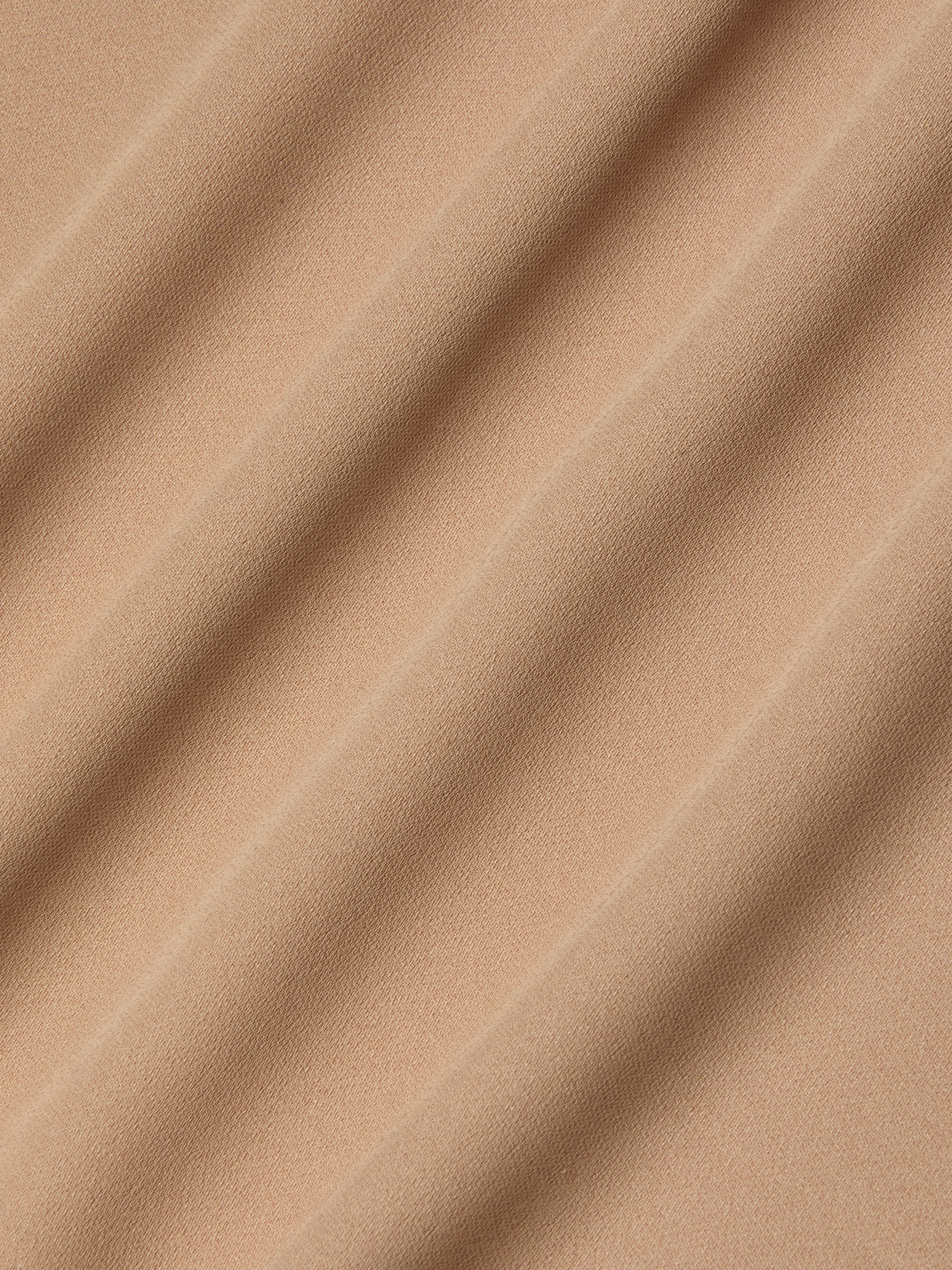 Close-up of beige poly georgette fabric with soft, diagonal waves and shadows, highlighting its smooth texture and gentle folds—an ideal choice for the Raye Slip Lining Dress featuring adjustable straps.