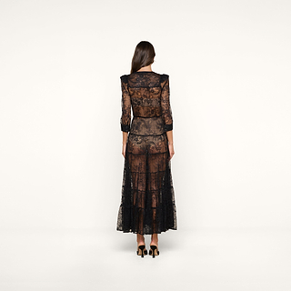 A woman stands facing away, wearing the Seraphina Lace Tiered Maxi Dress with 3/4 length sleeves and black heels, against a plain white background.