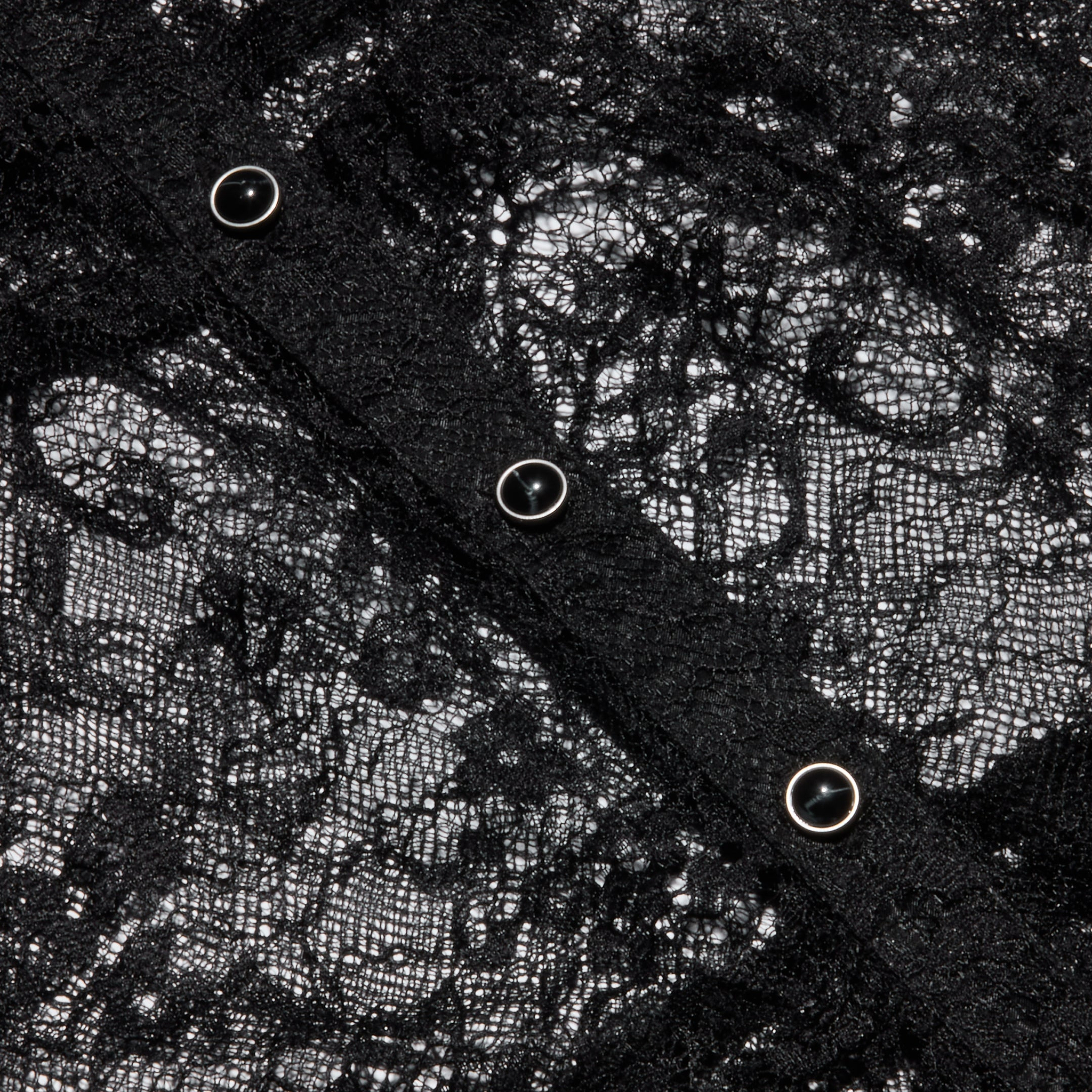 Close-up of the Seraphina Lace Tiered Maxi Dress, featuring intricate black sheer lace fabric with four metallic snap buttons arranged diagonally across the material, highlighting the delicate floral pattern and fine texture.
