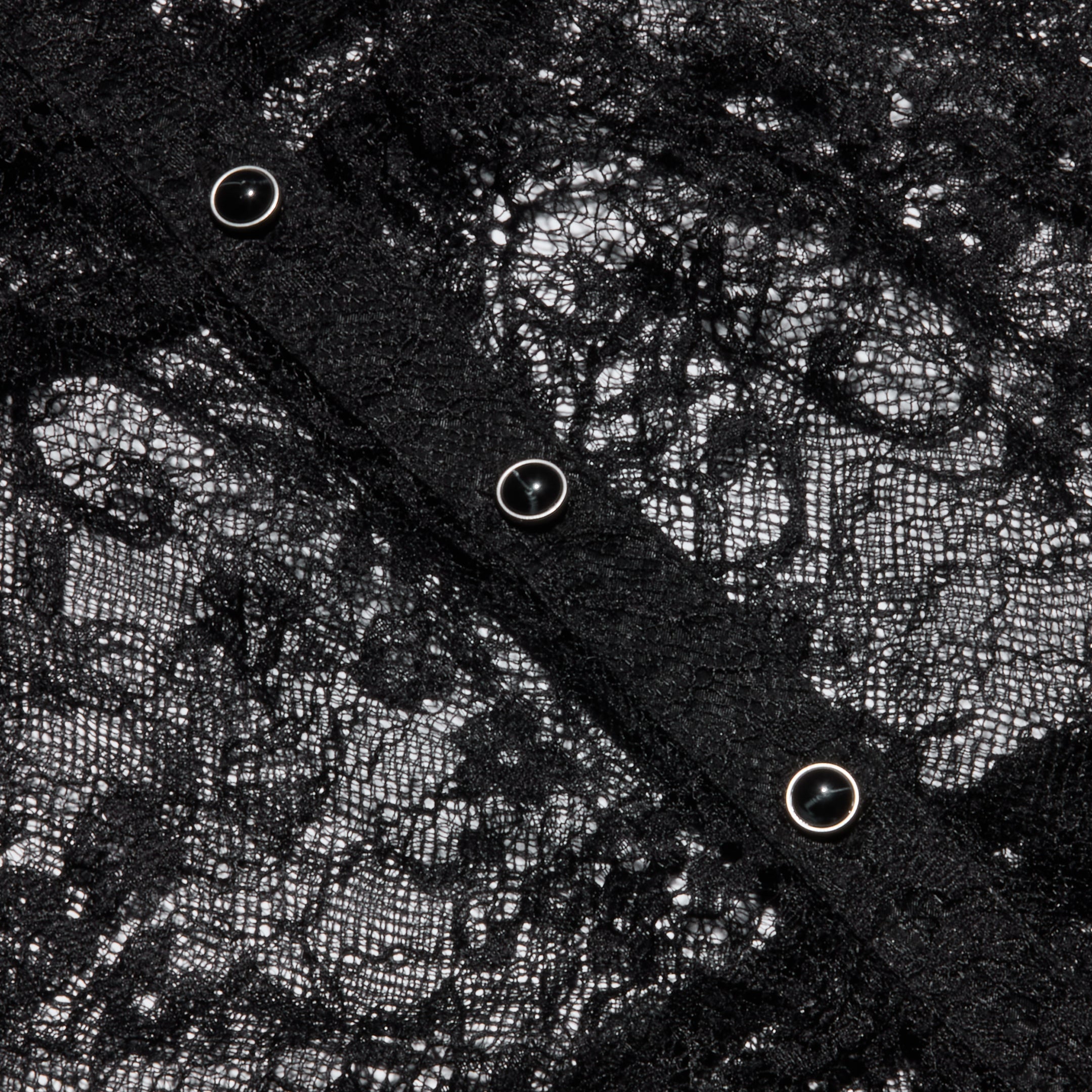 Close-up of the Seraphina Lace Tiered Maxi Dress, featuring intricate black sheer lace fabric with four metallic snap buttons arranged diagonally across the material, highlighting the delicate floral pattern and fine texture.