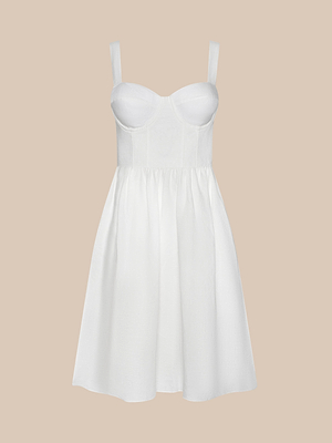 The Tiani Bustier Dress is a sleeveless white mini dress with underwire cups, wide straps, and a fitted bodice. Its gently flared skirt adds charm, and it’s showcased against a light beige background.