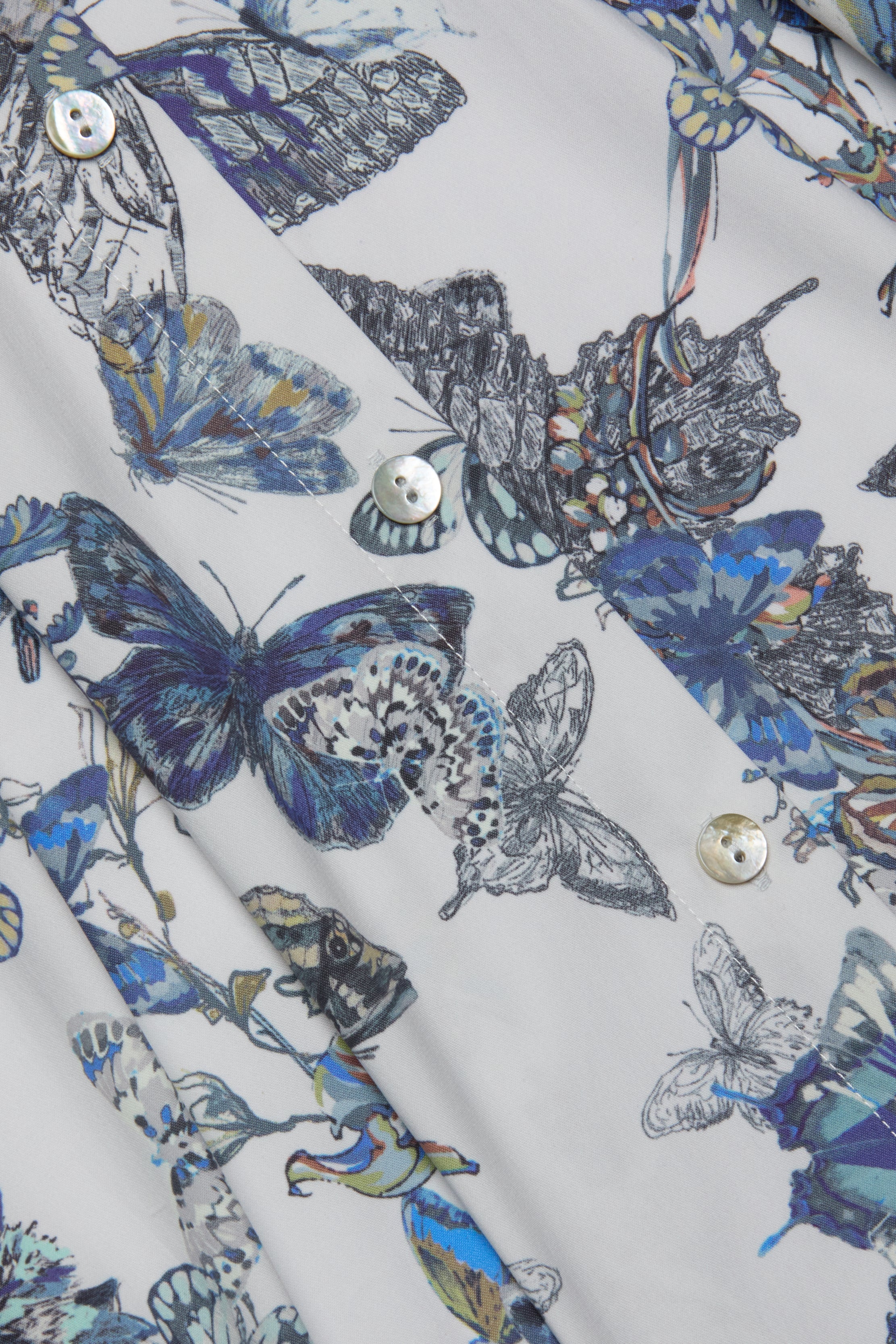 Close-up of the Journi Shirt Dress fabric, a stretch cotton blend featuring a detailed butterfly print with blue butterflies and moths, and pearly buttons visible in the foreground.