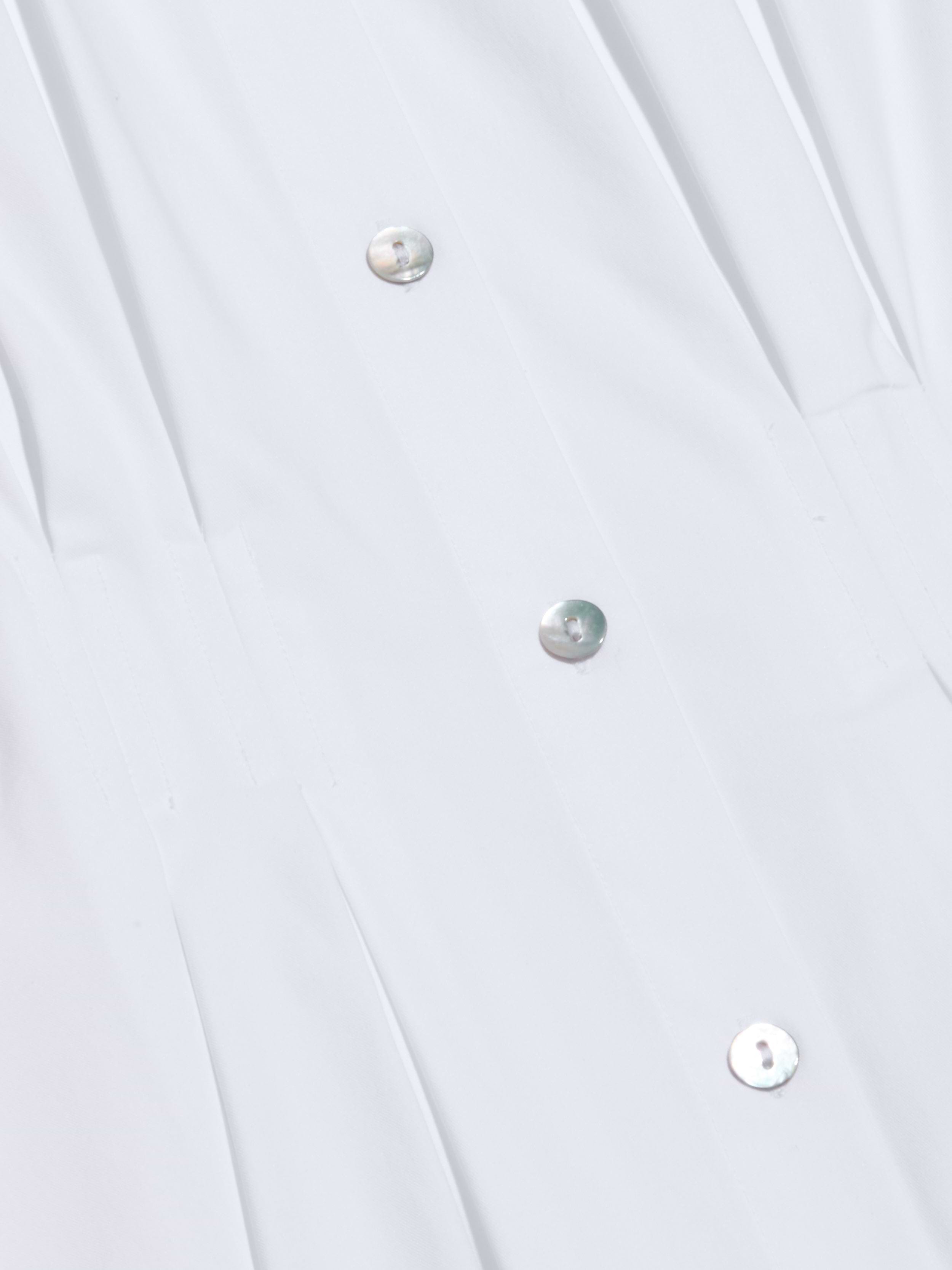 Close-up of the Journi Shirt Dress crafted from white cotton-blend poplin, featuring metallic buttons arranged in a vertical row. The smooth fabric is gently pleated near the buttons, creating a timeless silhouette.