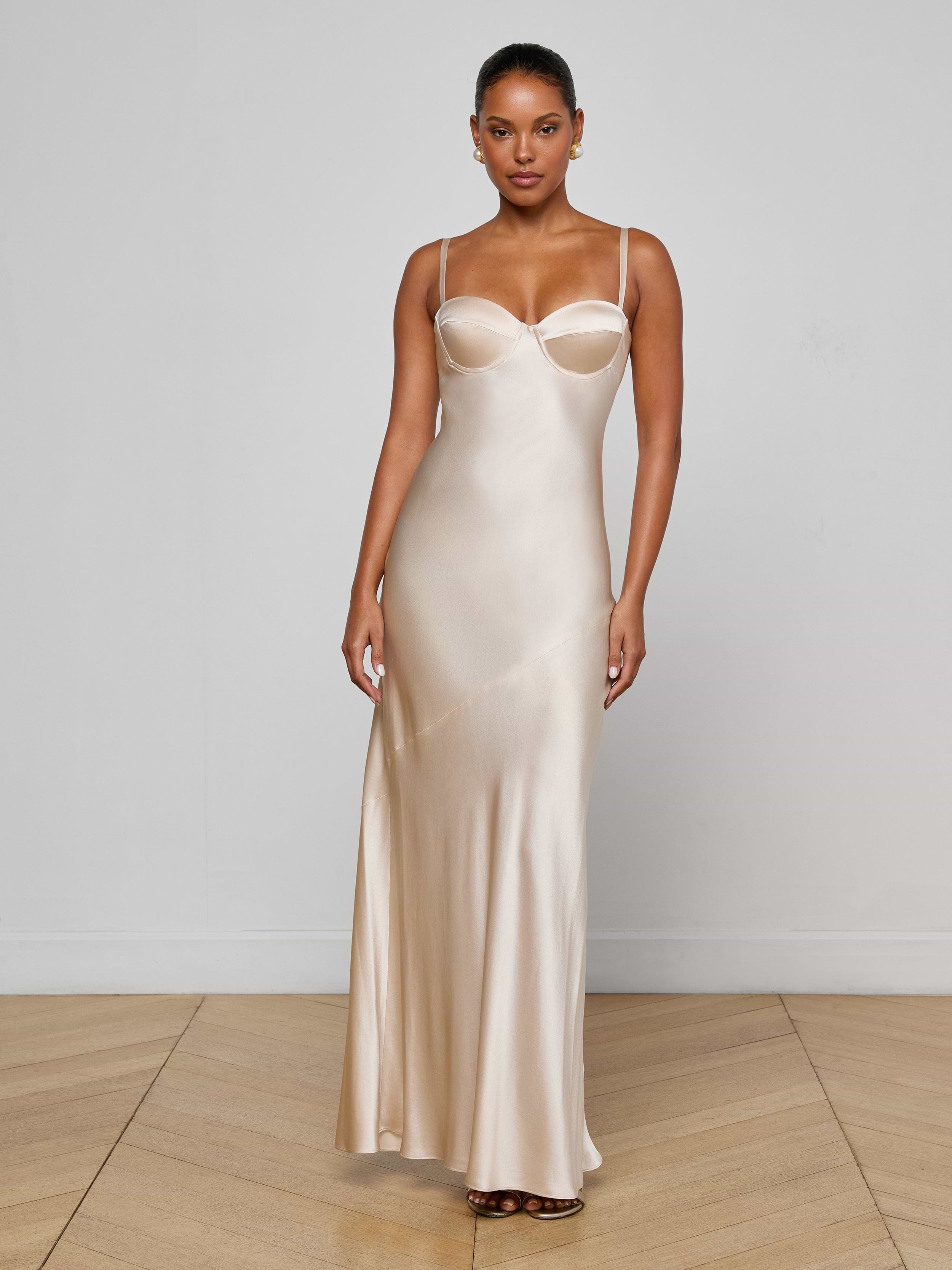A woman stands against a plain white background, wearing the Sayla Silk Gown—a long, sleeveless champagne dress with thin straps and a fitted bodice that evokes vintage glamour.