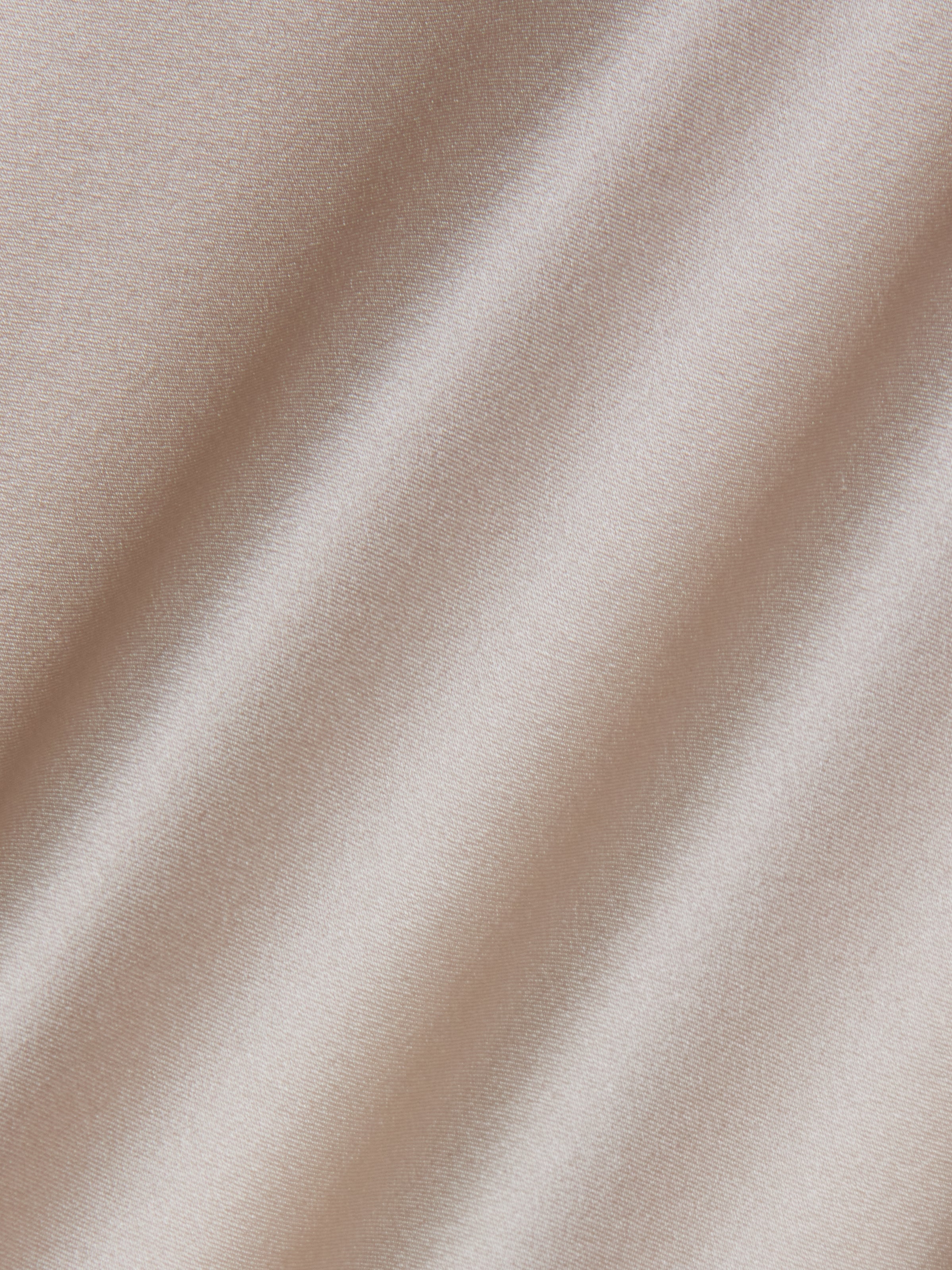 Close-up of the Sayla Silk Gown’s pale champagne-colored satin fabric, featuring soft diagonal folds and a smooth, shiny, and reflective texture that evokes the elegance of vintage glamour.