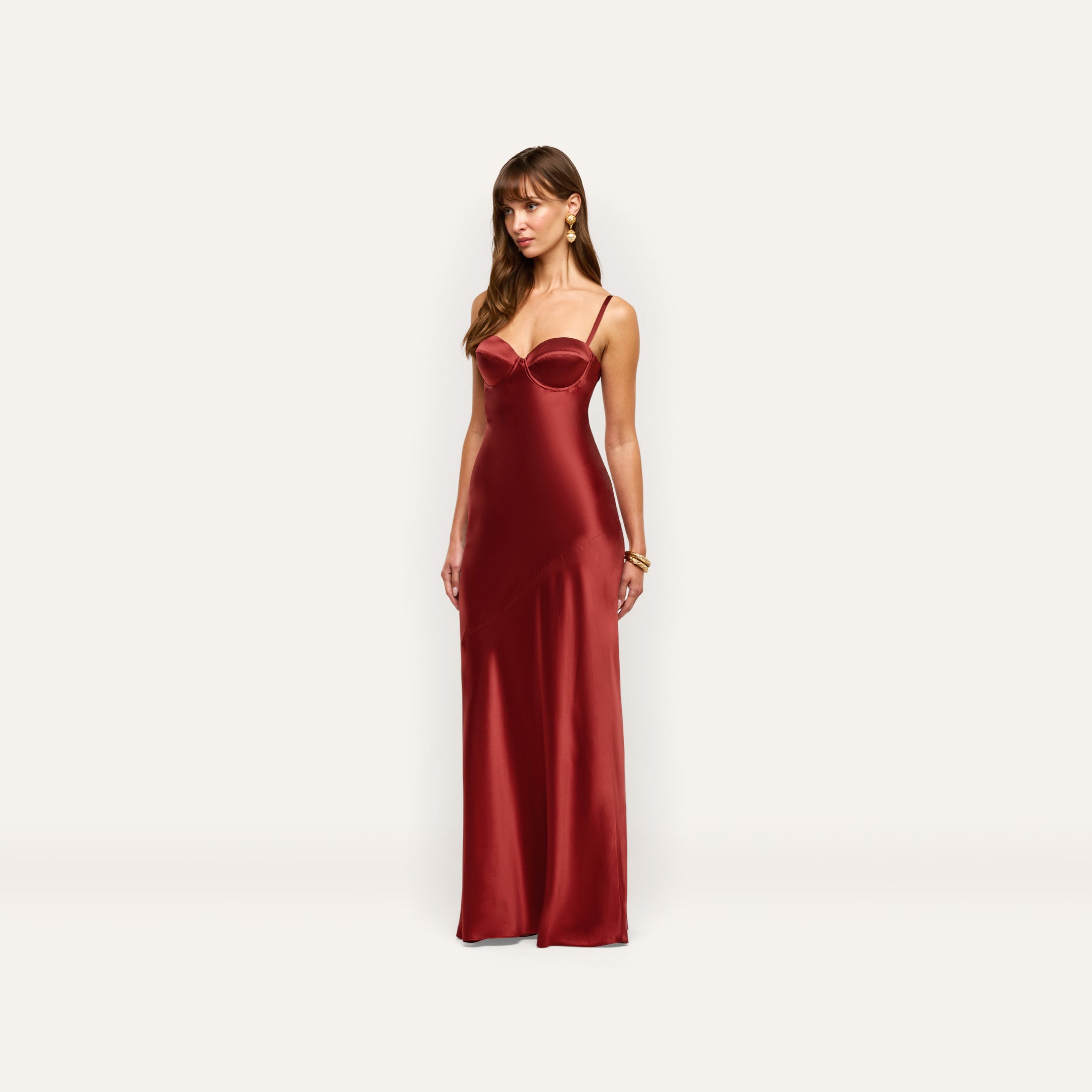A woman wearing a floor-length, sleeveless maroon Sayla Silk Gown featuring a vintage glamour corset-style bodice.