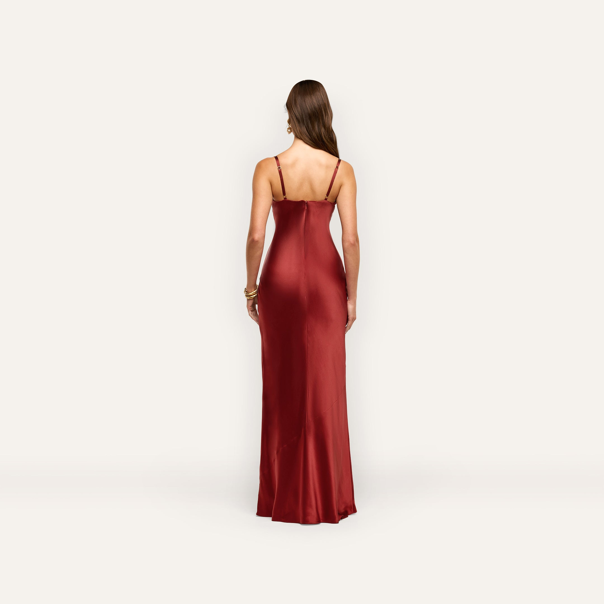A person seen from behind, wearing a floor-length, burgundy Sayla Silk Gown with spaghetti straps that evokes vintage glamour.
