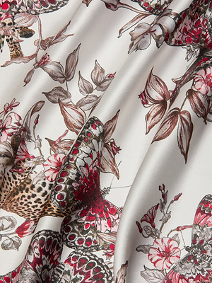 A close-up of smooth white fabric with a butterfly jungle print—delicate butterflies, flowers, and leopard spots—shows the softly draped folds that make the Sayla Silk Gown perfect for your next special event.