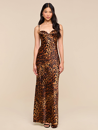 A woman wearing the Sayla Silk Gown—a long, sleeveless leopard print dress featuring spaghetti straps and subtle underwire cups—stands against a plain beige background.