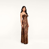 A woman stands in the Sayla Silk Gown—a full-length, sleeveless dress with thin straps and a leopard print—posing against a plain white background, creating an event-ready look.