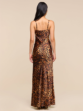 A woman with long dark hair wears the Sayla Silk Gown—a sleeveless, floor-length leopard print silk dress with thin straps—standing facing away on a plain beige background.