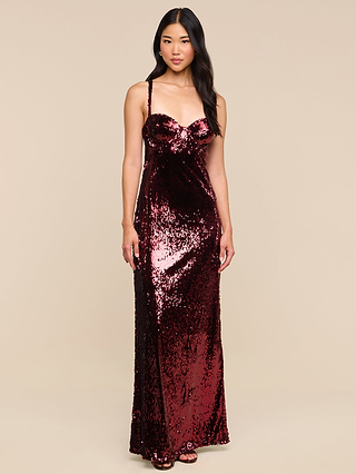 Wearing the Sayla Sequin Gown—a floor-length, sleeveless, dark red silk dress adorned with shimmering sequins and delicate thin straps—a woman stands against a plain beige background, exuding timeless vintage glamour.