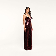 The woman stands facing forward against a plain white background, wearing the sleeveless, floor-length Sayla Sequin Gown in burgundy, a dress that exudes vintage glamour.