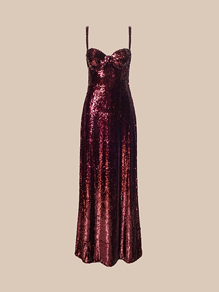 The Sayla Sequin Gown, a sleeveless dress in deep red sequins featuring thin straps and a fitted bodice, exudes vintage glamour as it is elegantly displayed against a plain beige background.