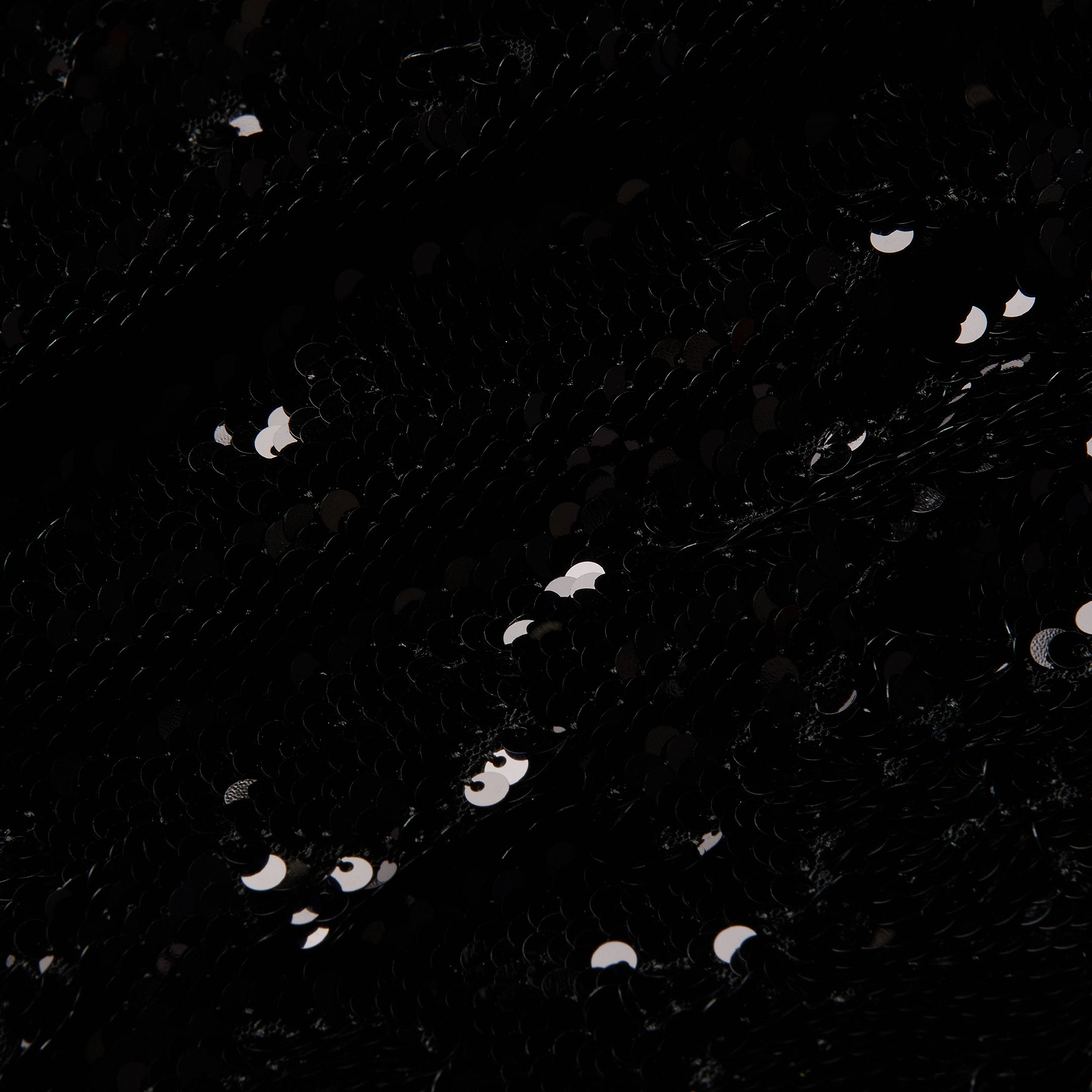 Close-up of black fabric on the Sayla Sequin Gown, covered with shiny black sequins reflecting small spots of light, creating a textured and sparkling effect reminiscent of vintage glamour.