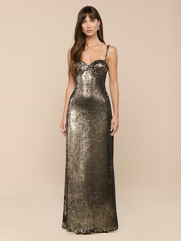 Une femme aux longs cheveux bruns et à lexpression calme se tient sur un fond neutre. Elle porte la robe à paillettes Sayla, une robe vert olive longue comme le sol, avec de fines bretelles, un corsage ajusté et un style glamour vintage.