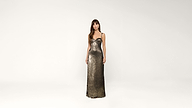 A woman in a metallic, floor-length, fitted sequin gown stands against a plain white background, looking forward with relaxed arms at her sides.