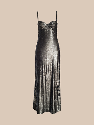 The Sayla Sequin Gown, a sleeveless metallic silver slip dress with thin spaghetti straps and a sweetheart neckline, radiates vintage glamour against a plain beige background.