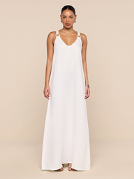 A woman stands against a plain white background wearing the Didi Maxi Dress—a long, sleeveless maxi dress featuring adjustable straps and silver embellishments on the shoulders. Her hair is pulled back, and she accessorizes with hoop earrings and sandals.